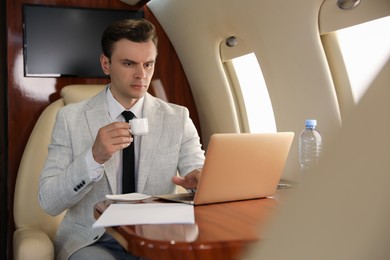 Businessman with cup of coffee working on laptop at table in airplane during flight