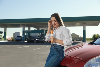 Photo of Beautiful young woman with hot dog near car at gas station. Space for text