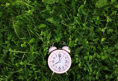 Pink small alarm clock on green grass outdoors, top view. Space for text