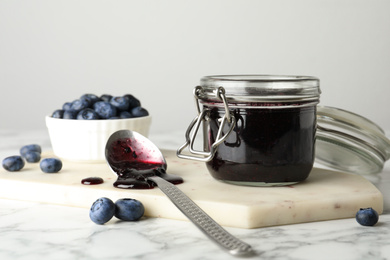 Jar of blueberry jam and fresh berries on white marble table