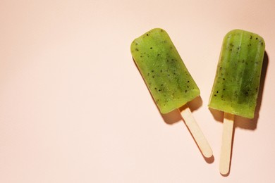 Tasty kiwi ice pops and space for text on pale light pink background, top view. Fruit popsicle