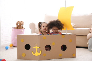 Photo of Cute little children playing with cardboard ship at home