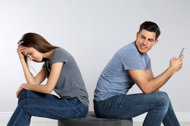 Man with smartphone mocking his girlfriend on grey background. Relationship problems