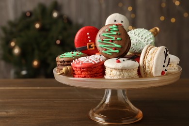 Photo of Stand with beautifully decorated Christmas macarons on wooden table against blurred festive lights