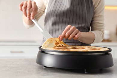 Photo of Woman cooking delicious crepe on electric pancake maker in kitchen, closeup