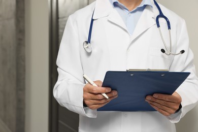 Doctor in white coat with stethoscope and clipboard indoors, closeup