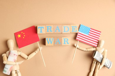 Wooden cubes with words Trade War, mannequins holding money and flags on beige background, flat lay