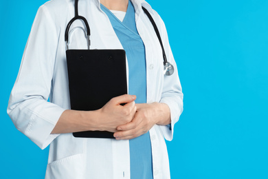 Doctor with stethoscope and clipboard on blue background, closeup