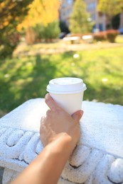 Photo of Woman with cardboard cup of coffee on stone bench outdoors, closeup