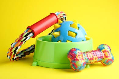 Feeding bowl and toys for pet on yellow background