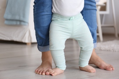 Baby doing first steps with mother's help, closeup of legs