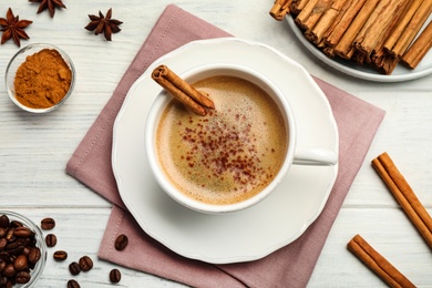Delicious hot coffee with cinnamon on white wooden table, flat lay