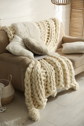 Beige sofa with knitted blanket and cushions in room. Interior design