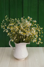 Photo of Beautiful bouquet of chamomiles in ceramic jug on white table against green wooden background
