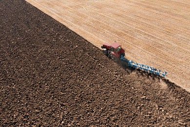 Tractor pulling plow in agricultural field on sunny day, aerial view