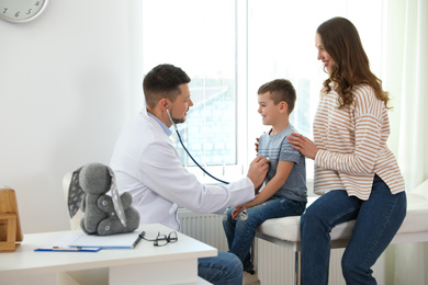 Photo of Mother and son visiting pediatrician. Doctor examining little patient with stethoscope in hospital