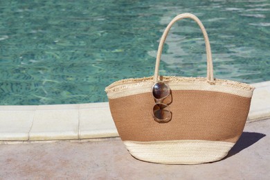 Photo of Stylish bag and sunglasses near outdoor swimming pool on sunny day, space for text. Beach accessories