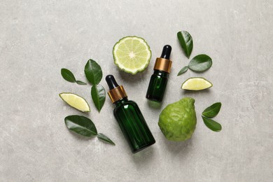 Glass bottles of bergamot essential oil and fresh fruits on light table, flat lay