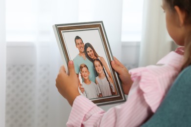 Little girl holding framed family photo indoors, closeup