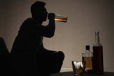 Addicted man drinking alcohol indoors, focus on table with bottles
