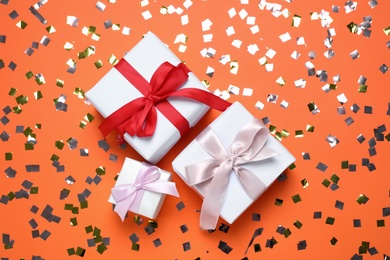 Different gift boxes and confetti on orange background, flat lay