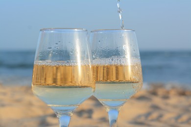 Pouring white wine into glasses on sandy seashore, closeup