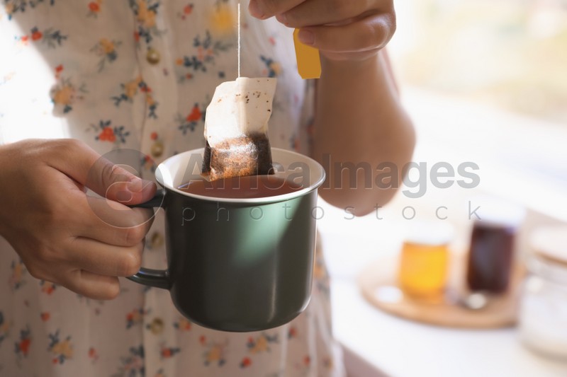 Woman taking tea bag out of cup indoors, closeup