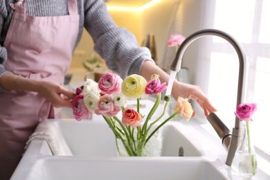 Woman taking care of cut fresh ranunculus flowers in kitchen, closeup