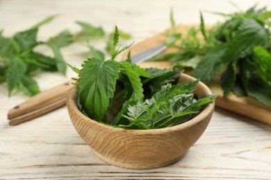 Photo of Fresh stinging nettle leaves in bowl on white wooden table