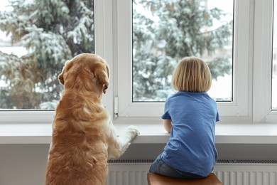 Photo of Cute little child with Golden Retriever near window at home, back view. Adorable pet