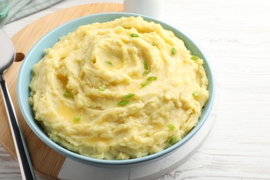 Bowl of tasty mashed potatoes with onion served on white wooden table, closeup