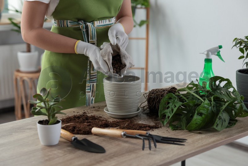 Woman filling flowerpot with drainage at table indoors, closeup. Houseplant care