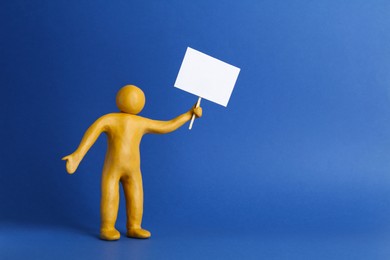 Human figure made of yellow plasticine holding blank sign on blue background. Space for text