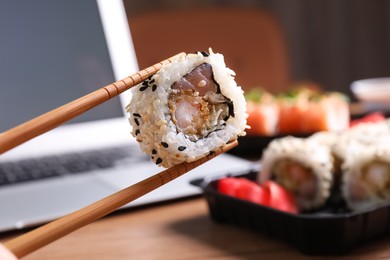 Holding sushi roll with chopsticks over table, closeup