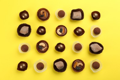 Photo of Different delicious chocolate candies on yellow background, flat lay
