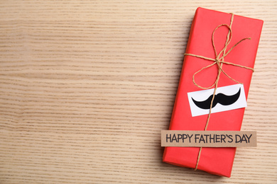 Photo of Gift box with mustache and words HAPPY FATHER'S DAY on wooden background, top view. Space for text