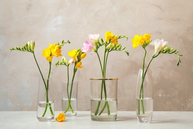 Beautiful blooming freesias in glass vases on table against grey background