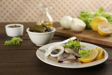 Photo of Sliced salted herring fillet served with lettuce, onion rings and lemon on wooden table