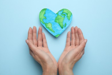 Woman with heart shaped model of planet on light blue background, top view. Earth Day