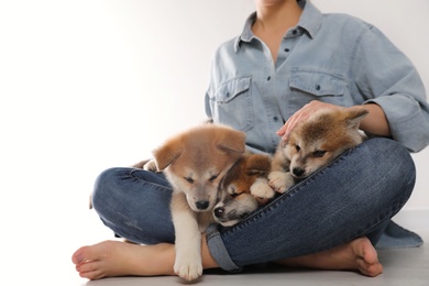 Woman with Akita Inu puppies sitting on floor near light wall, closeup