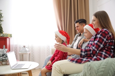 Family with children using video chat on laptop in room decorated for Christmas