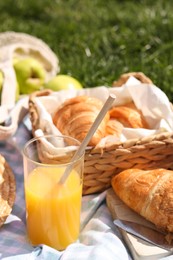 Blanket with juice and croissants for picnic on green grass, closeup