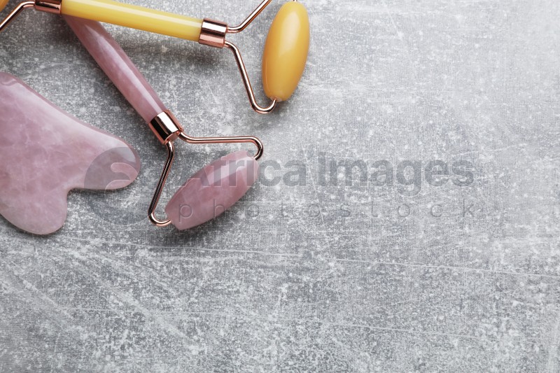 Quartz gua sha tool and face rollers on grey background, flat lay. Space for text