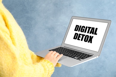 Woman holding laptop with phrase DIGITAL DETOX on light blue background, closeup