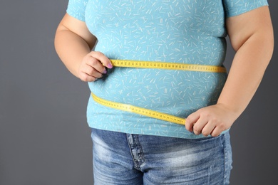 Overweight woman with measuring tape on gray background, closeup