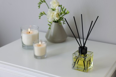 Aromatic reed air freshener, freesia flowers and candles on white bedside table indoors