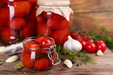 Glass jar of pickled cherry tomatoes on wooden table. Space for text