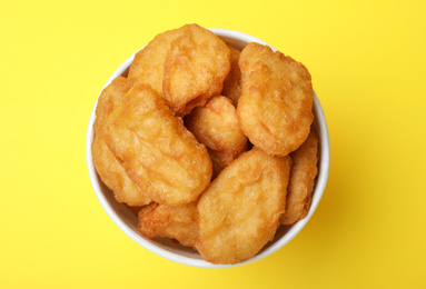 Photo of Bucket with tasty chicken nuggets on yellow background, top view