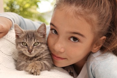 Photo of Cute little girl with kitten on white blanket at home, closeup. Childhood pet