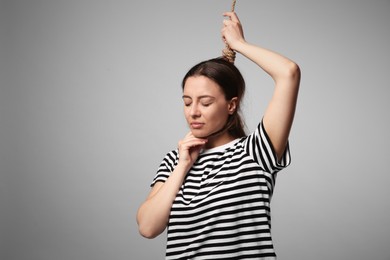 Depressed woman with rope noose on neck against light grey background